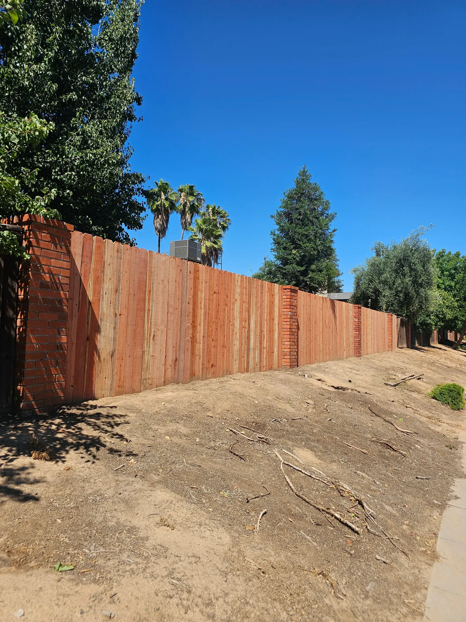 A finished redwood fence running the length of a property line between brick pillars, seen from the neighbouring lot.