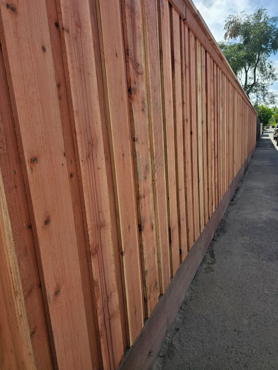A tall redwood fence running the length of a Fresno side yard in full sun.