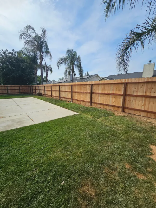 A framed wood fence enclosing a green back lawn, with palms behind the fence line.