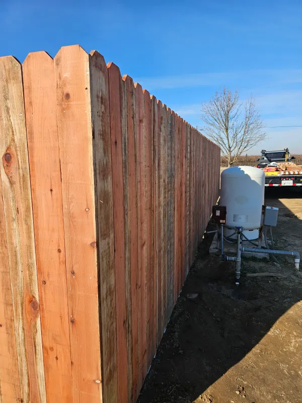 A newly built redwood fence with the pickets still bright, seen down the property line.