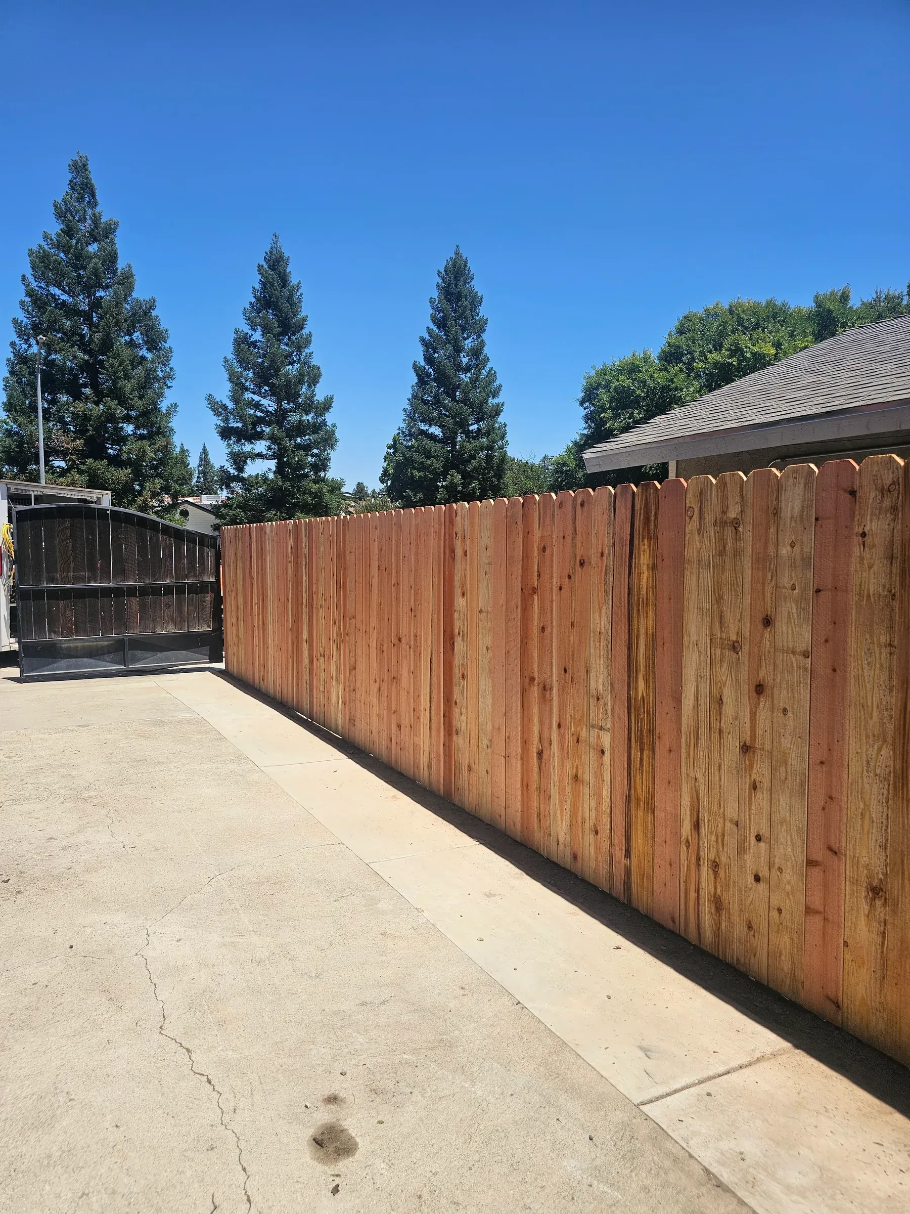 A tall dog-ear privacy fence running the length of a driveway with no gaps between pickets.
