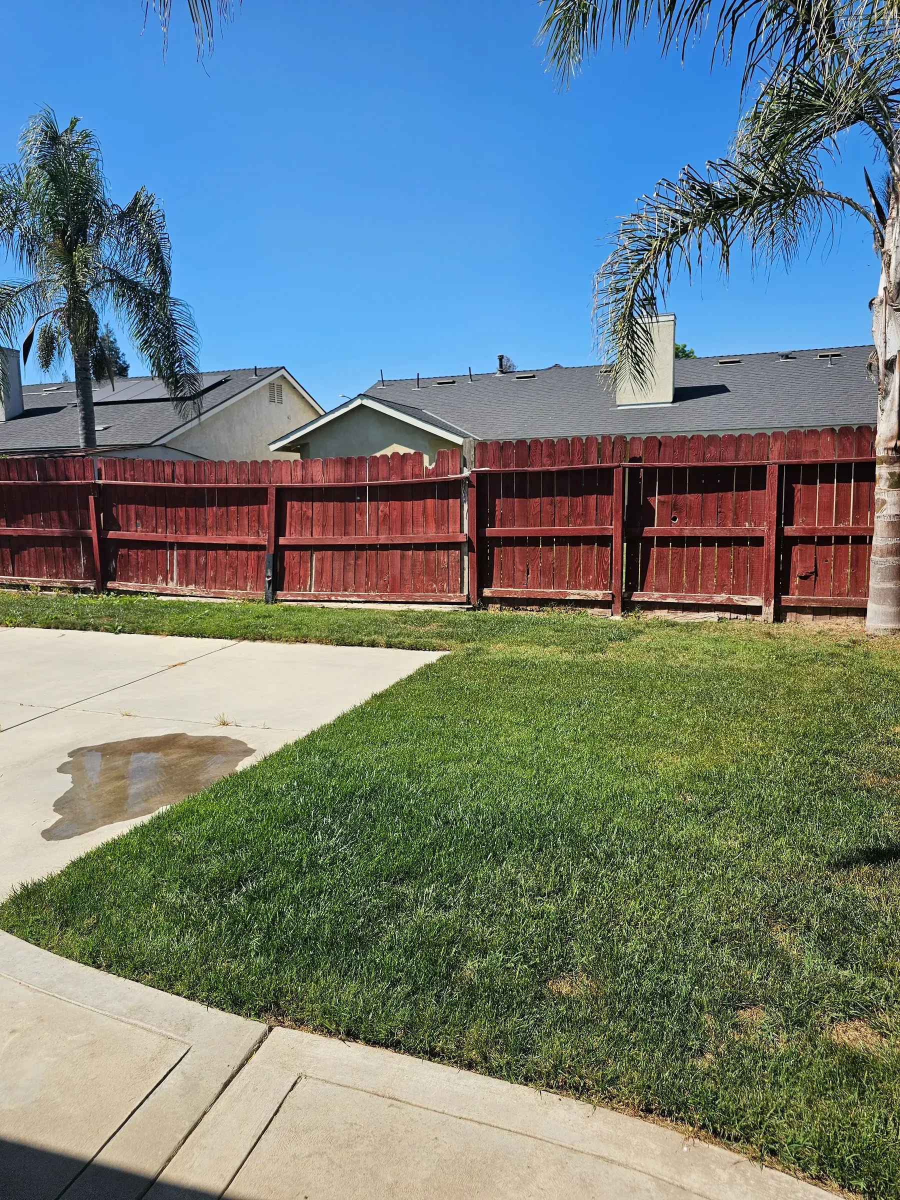 A wood fence carrying an even dark red stain across every picket, beside a green lawn.