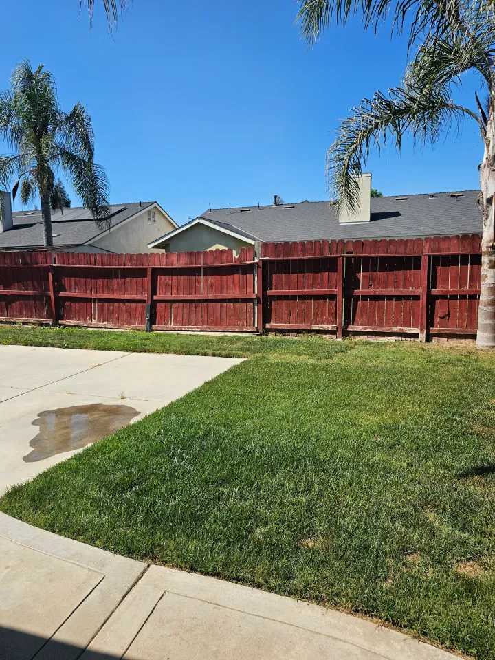 A wood fence carrying an even dark red stain across every picket, beside a green lawn.