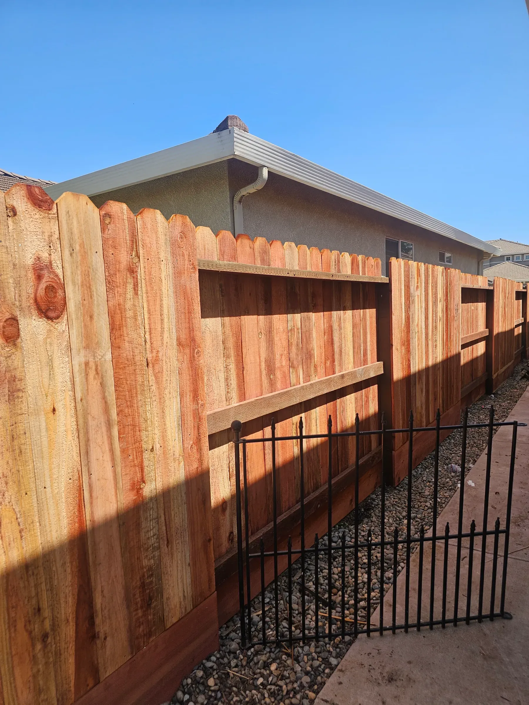 A wrought iron panel set into a wood fence line beside a house.